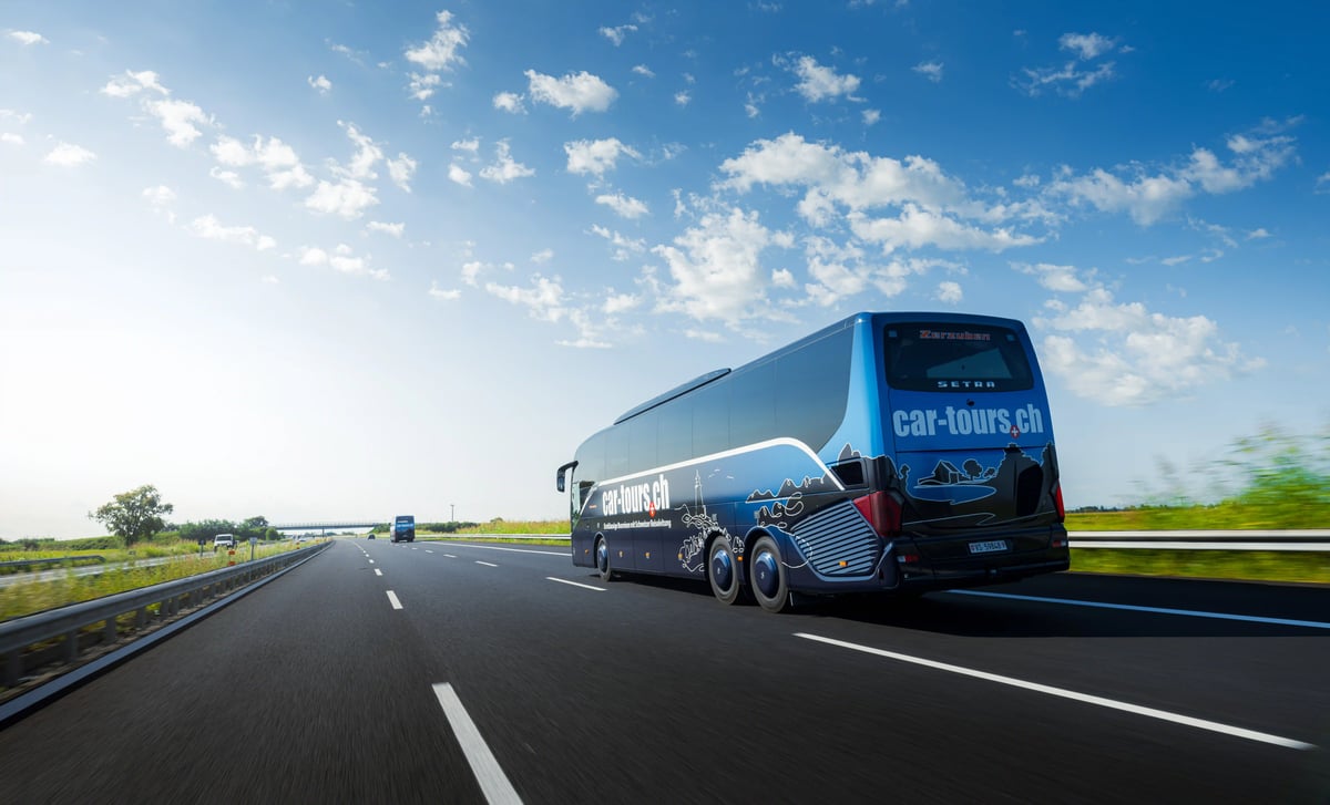 Un autocar moderne roule sur une autoroute dégagée à travers un paysage plat sous un ciel bleu parsemé de nuages blancs