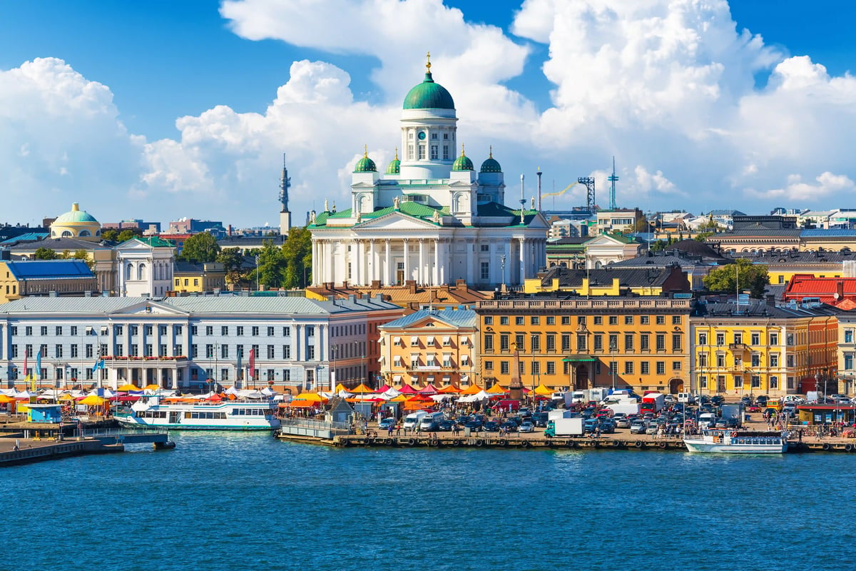 Blick auf den Dom von Helsinki mit grüner Kuppel, umliegenden historischen Gebäuden und belebtem Hafenbereich am Wasser