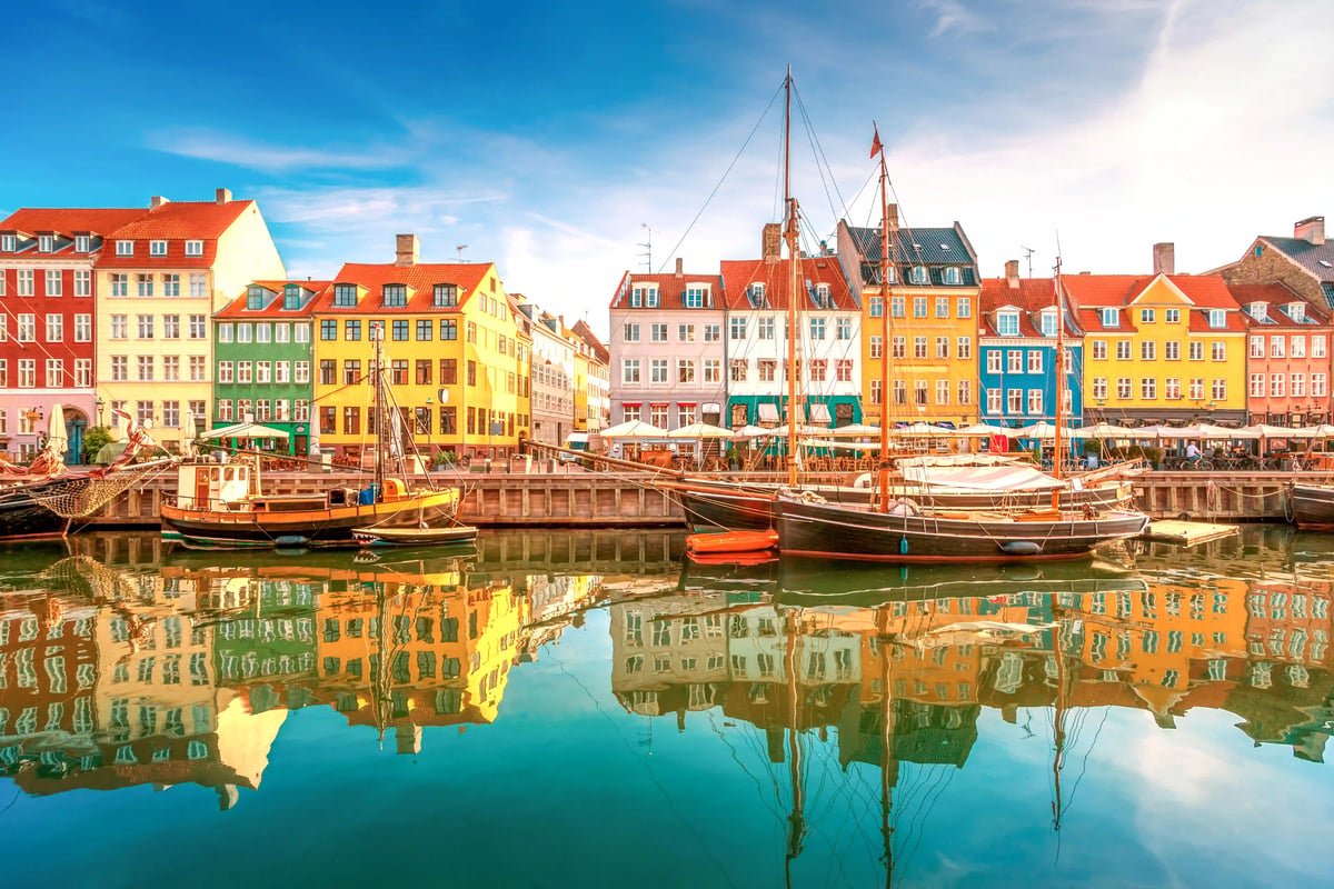 Blick auf den Hafen Nyhavn in Kopenhagen mit bunten Giebelhäusern, historischen Segelschiffen und Spiegelungen im ruhigen Wasser