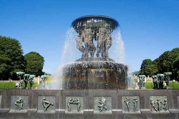 Monumentaler Brunnen mit nackten Bronzefiguren und fliessendem Wasser im Vigeland-Park in Oslo unter blauem Himmel