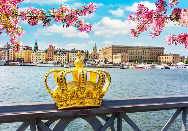 Goldene Krone auf einem Brückengeländer mit Blick auf Wasser, Altstadt und Frühlingsblüten in Stockholm