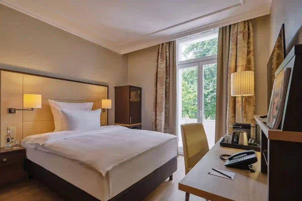 Helles Hotelzimmer mit Doppelbett, Schreibtisch, Fenster und Blick ins Grüne