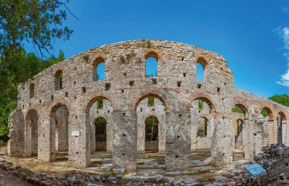 Ruinen des antiken Theaters von Butrint mit steinernen Bögen und archäologischer Ausgrabungsstätte.