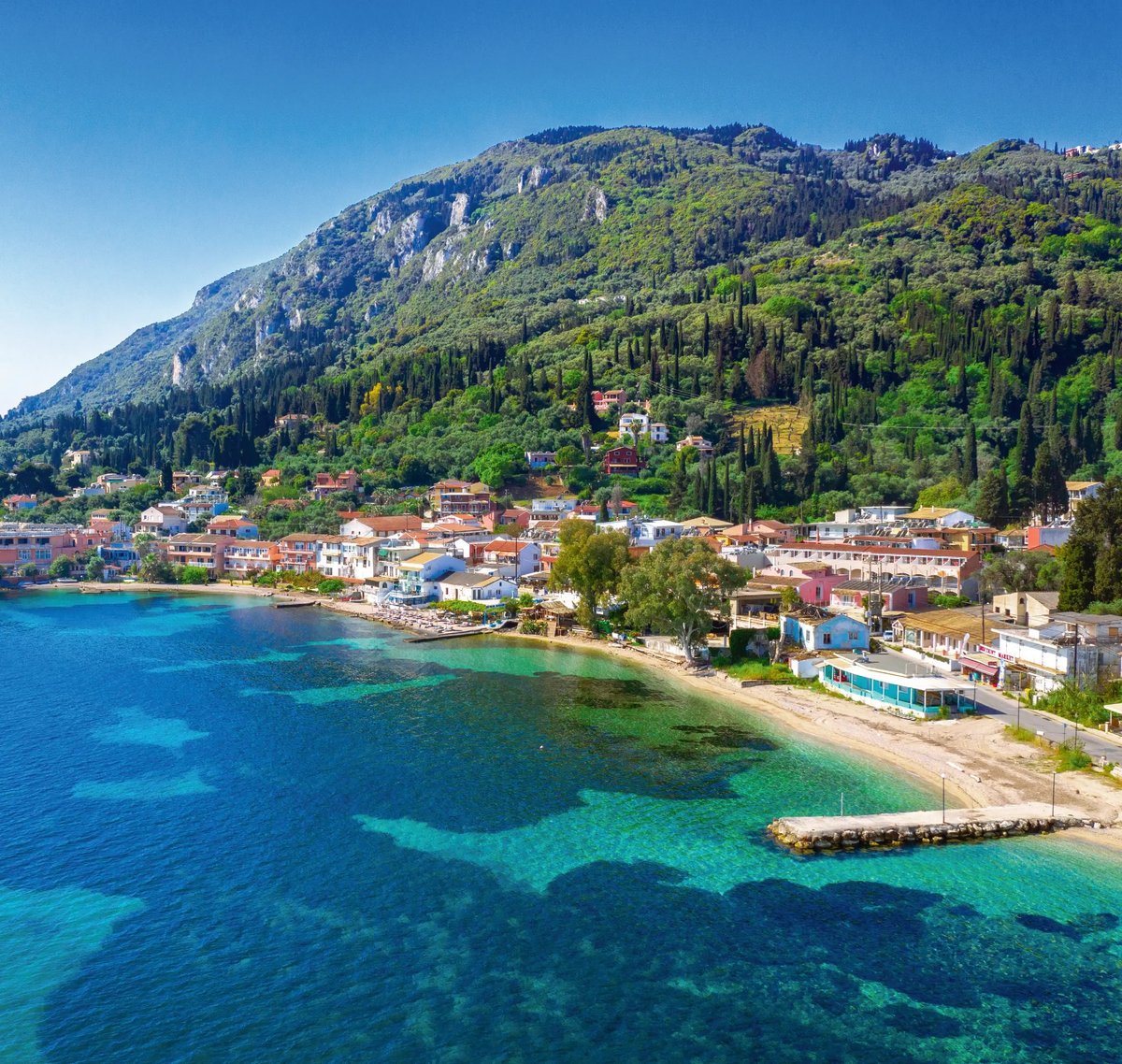 Küstenort an der Albanischen Riviera mit türkisblauem Meer, Strand und grünen Berghängen.