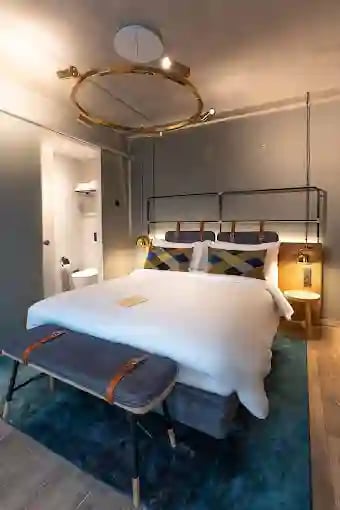 Stilvolles Hotelzimmer mit großem Bett, Sitzbank am Fußende, Nachttischlampen und schlichter, moderner Einrichtung.