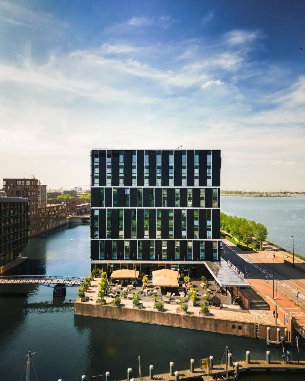 Aussenansicht des Hotels Four Elements in Amsterdam mit blauem Himmel und am Wasser.