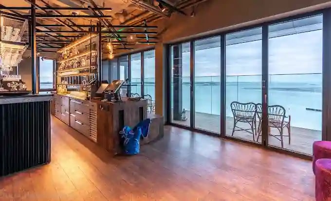 Moderne Skybar mit Bartresen, Sitzgelegenheiten und bodentiefen Fenstern mit Blick auf das Wasser