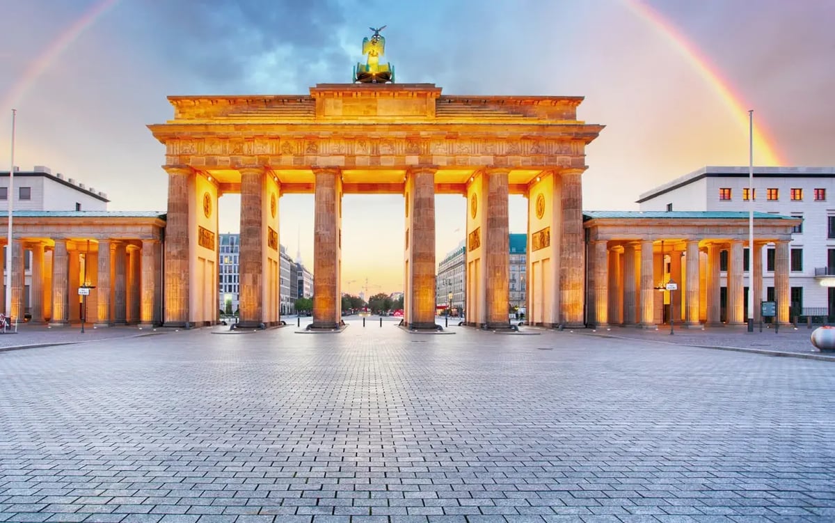 Brandenburger Tor in Berlin bei Abendlicht mit Regenbogen über dem Wahrzeichen.