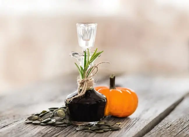 Flasche mit steirischem Kürbiskernöl, Kürbis und Kürbiskernen auf einem Holztisch.