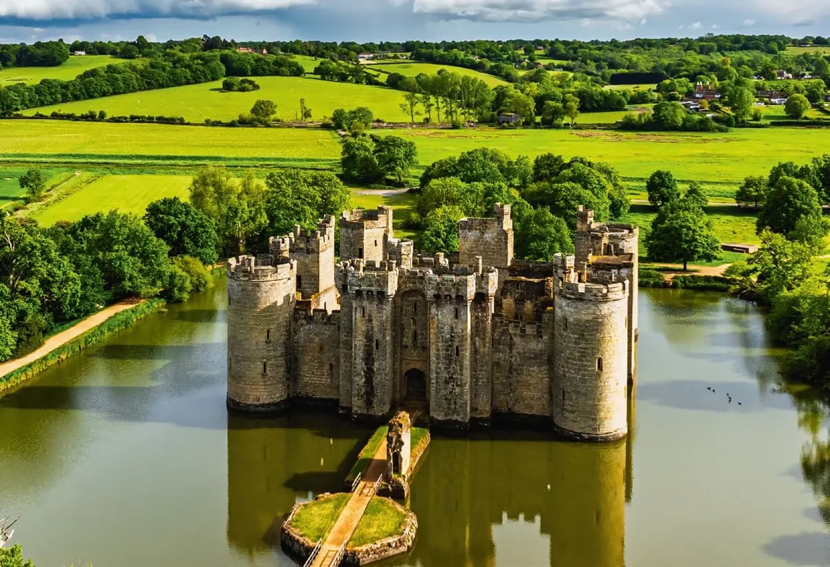 Mittelalterliche Wasserburg Bodiam Castle, umgeben von einem Wassergraben und grüner Landschaft.