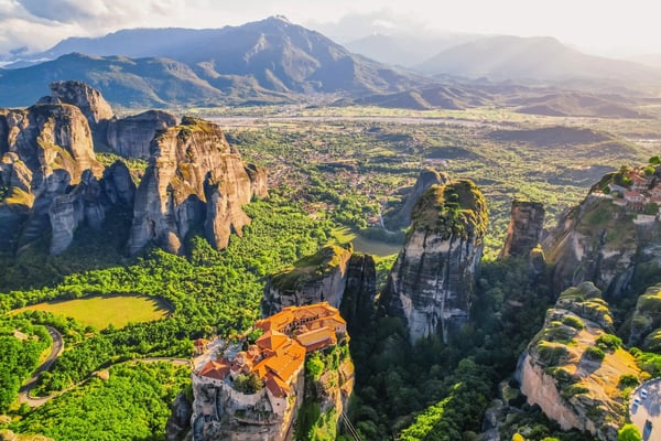 Meteora Klöster auf hohen Felsformationen mit grünem Tal und Bergen im Hintergrund