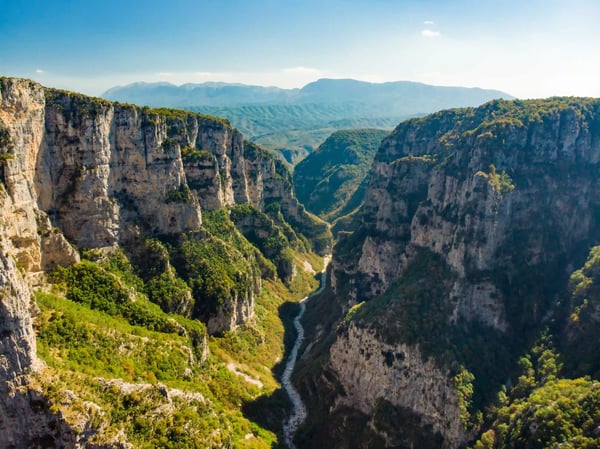 Tiefe Vikos Schlucht mit steilen Felswänden, grünen Hängen und schmalem Flusslauf im Tal