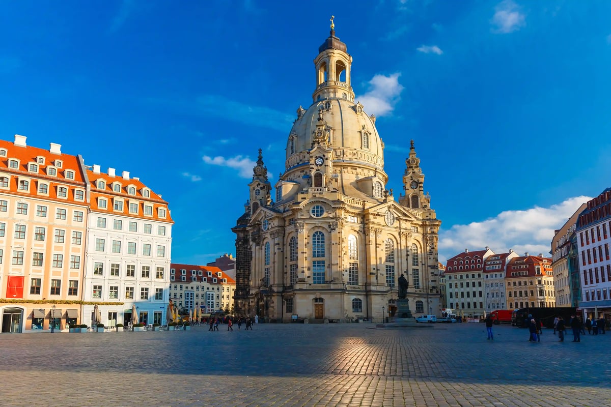 Blick auf die Frauenkirche in Dresden mit markanter Kuppel, umgeben von historischen Gebäuden auf einem grossen Stadtplatz bei blauem Himmel
