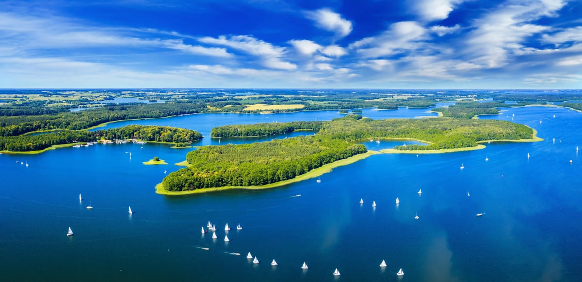 Luftaufnahme der Masurischen Seenplatte mit verzweigten Seen, grünen Inseln und zahlreichen Segelbooten unter blauem Himmel
