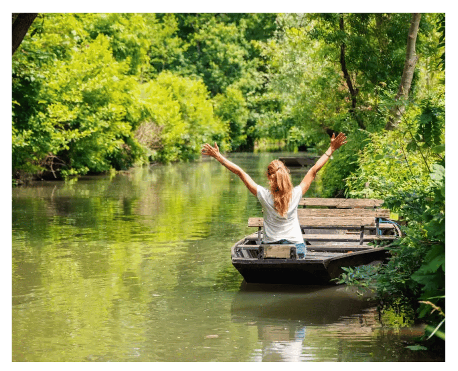 Fröhliche Reisende geniesst eine Bootsfahrt durch die grüne Flusslandschaft des Marais Poitevin.
