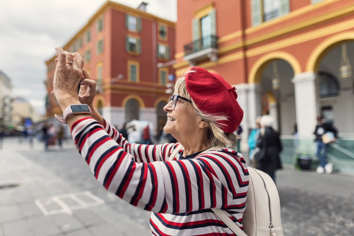 Ältere Frau mit roter Mütze fotografiert eine Stadtansicht auf einem Platz mit Arkadengebäuden