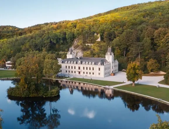 Schloss Hernstein mit Parkanlage und See, eingebettet in bewaldete Hügel.