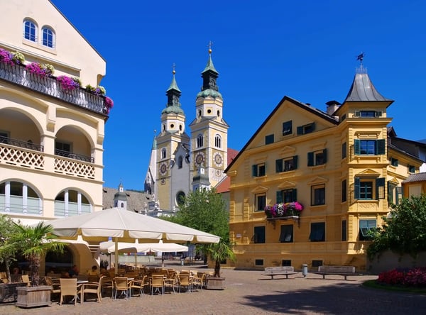 Historische Altstadt von Brixen mit bunten Häusern, Cafe Terrasse und Domtürmen unter blauem Himmel
