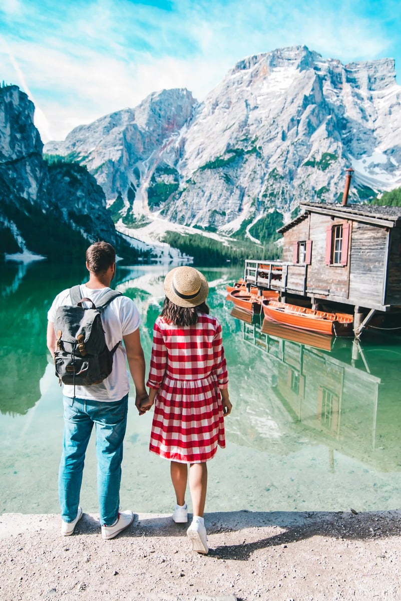 Paar steht am Ufer des Pragser Wildsees und blickt auf türkisfarbenes Wasser, Holzboote und Berglandschaft