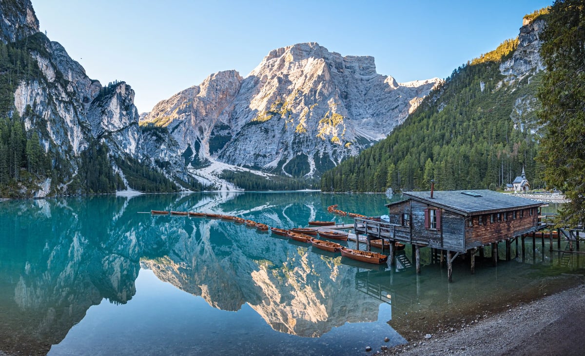 Weiter Blick über den ruhigen Pragser Wildsee mit klarer Spiegelung der Dolomiten und Bootssteg