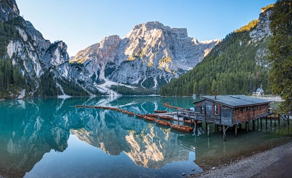 Weiter Blick über den ruhigen Pragser Wildsee mit klarer Spiegelung der Dolomiten und Bootssteg