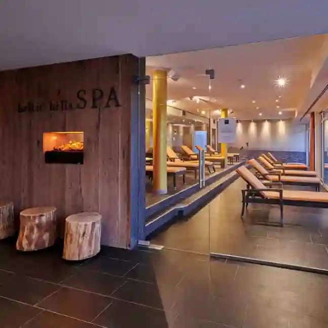 Moderner Spa und Wellnessbereich mit Liegenreihen, warmem Licht, Holzwaenden, Kamin und ruhiger Atmosphaere hinter einer Glasfront