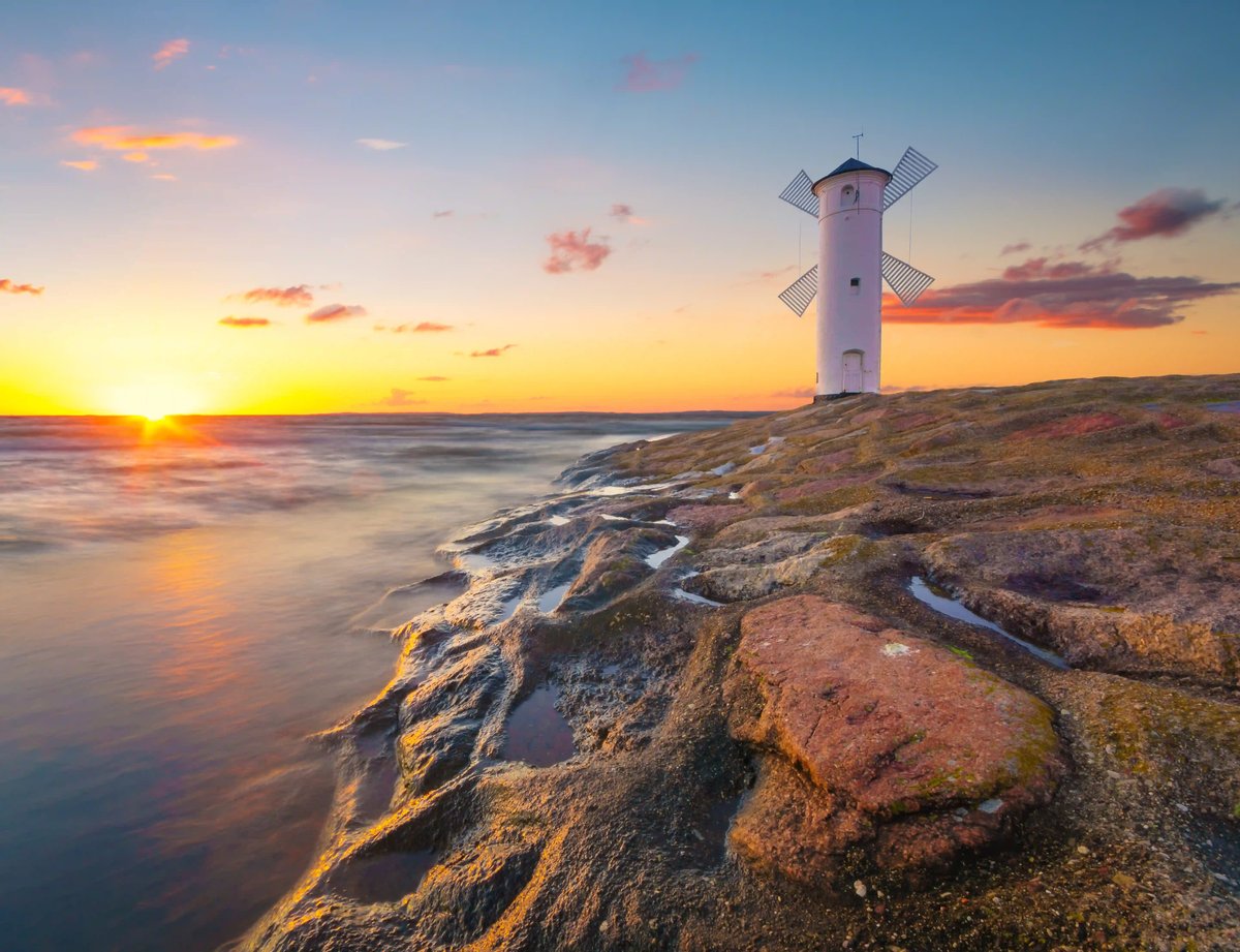 Weisse Windmühle auf Felsen an der Ostsee bei Sonnenuntergang und ruhigem Meer