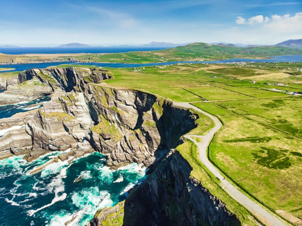 Küste in Irland mit steilen Klippen, Meeresbrandung und schmaler Strasse entlang der Felsen