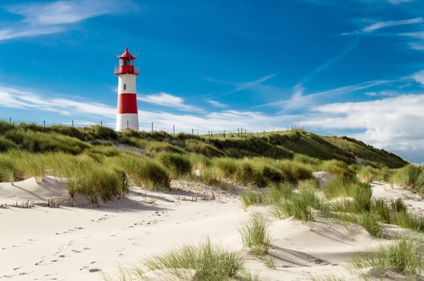 Dünenlandschaft auf Sylt mit rot weiss gestreiftem Leuchtturm, Sandstrand und Meer unter warmem Abendhimmel