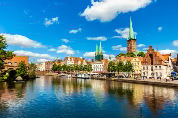 Altstadt von Lübeck mit bunten Häusern, Kirchtürmen und Spiegelung im Fluss bei sonnigem Wetter