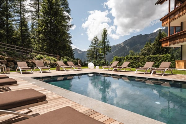 Beheiztes Aussenpool mit Liegen vor alpiner Bergkulisse in einem Südtiroler Hotel