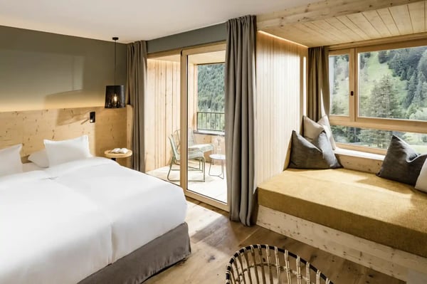 Modernes Hotelzimmer mit Doppelbett, Sitzbank, Holzelementen und Balkon mit Blick auf die Berglandschaft