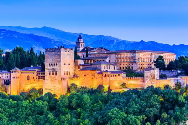 Alhambra in Granada mit beleuchteten Mauern vor Bergkulisse in der Abenddämmerung