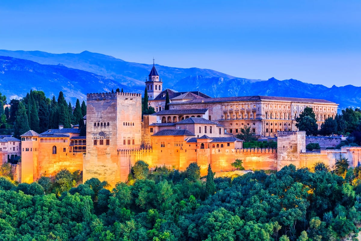 Alhambra in Granada mit beleuchteten Mauern vor Bergkulisse in der Abenddämmerung