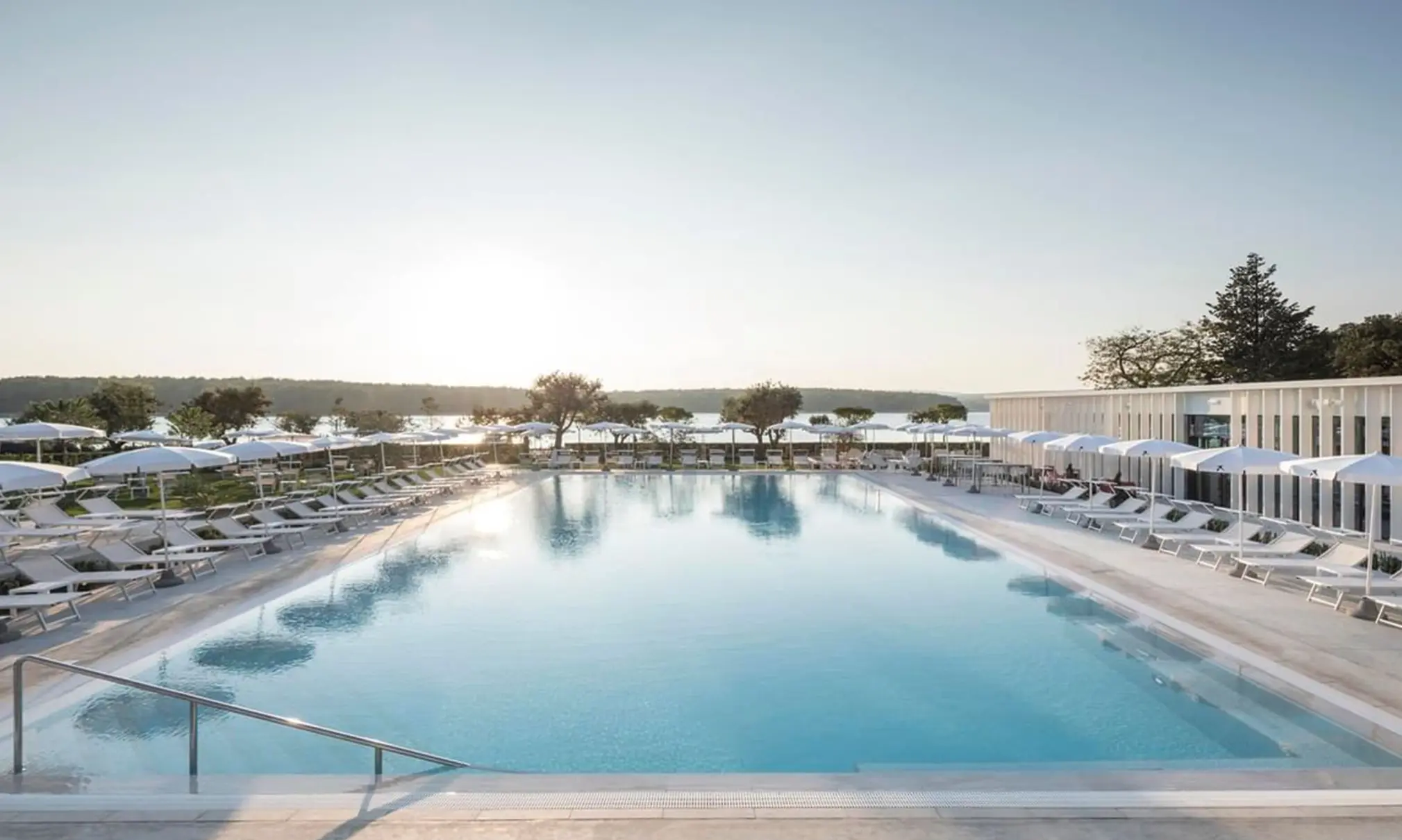 Moderner Hotelpool mit Liegen und Sonnenschirmen vor ruhiger Meereslandschaft bei Punat