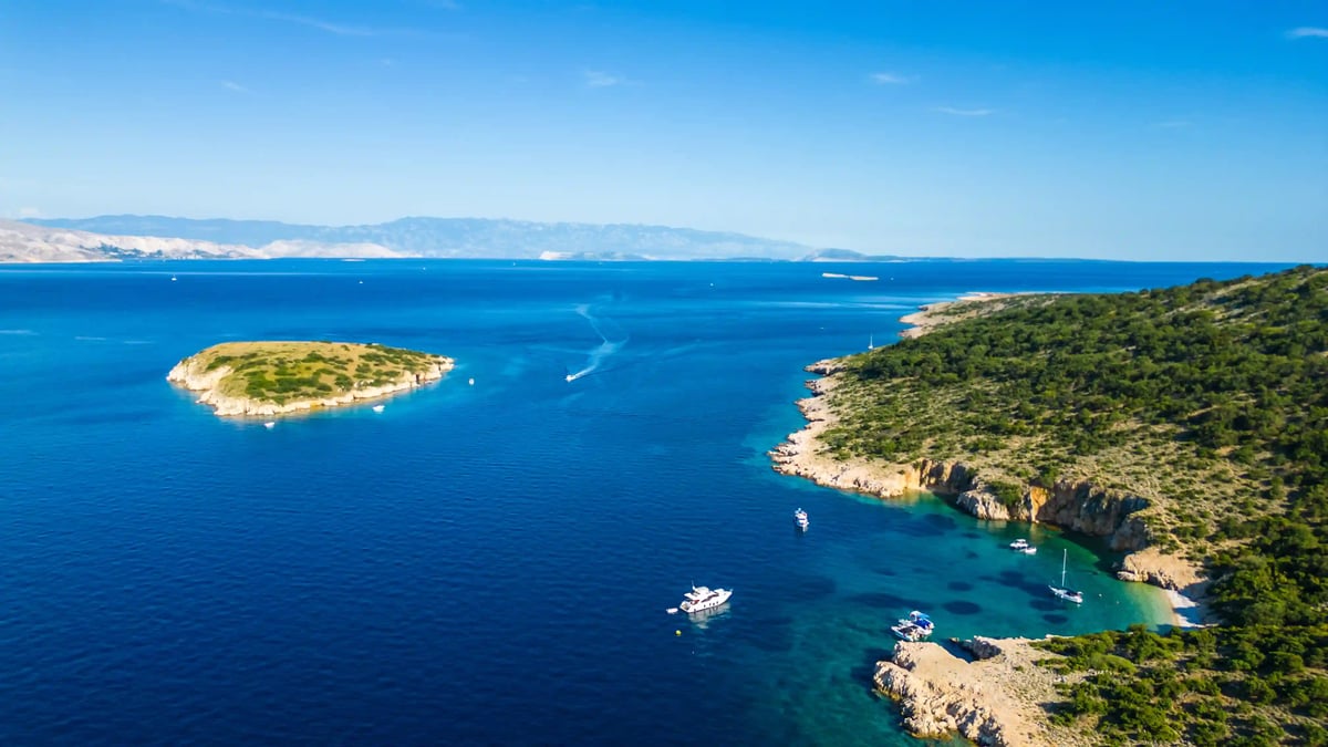 Luftaufnahme der Adria bei der Insel Plavnik mit blauem Meer, kleinen Booten und felsiger Küste
