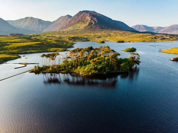 Berglandschaft im Connemara Nationalpark mit See, Felsen, grüner Vegetation und dramatischem Wolkenhimmel