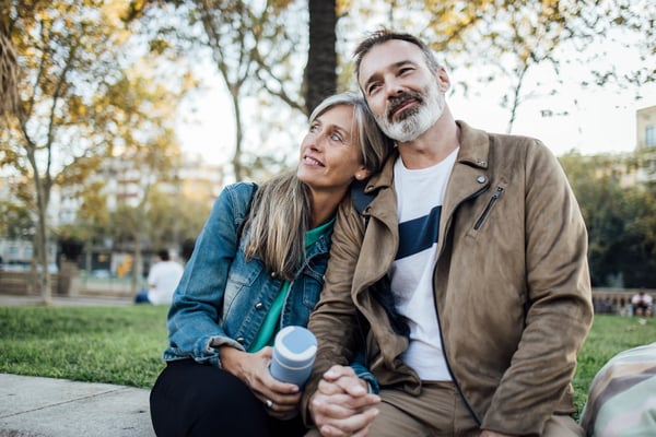 Paar sitzt entspannt im Park, hält sich an den Händen und blickt lächelnd in die Ferne