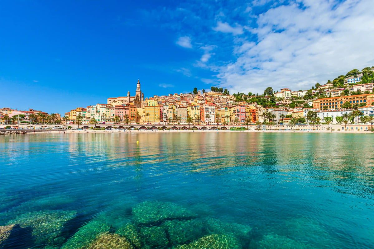 Blick auf die Altstadt von Menton mit pastellfarbenen Gebäuden am Mittelmeer bei Sonnenschein