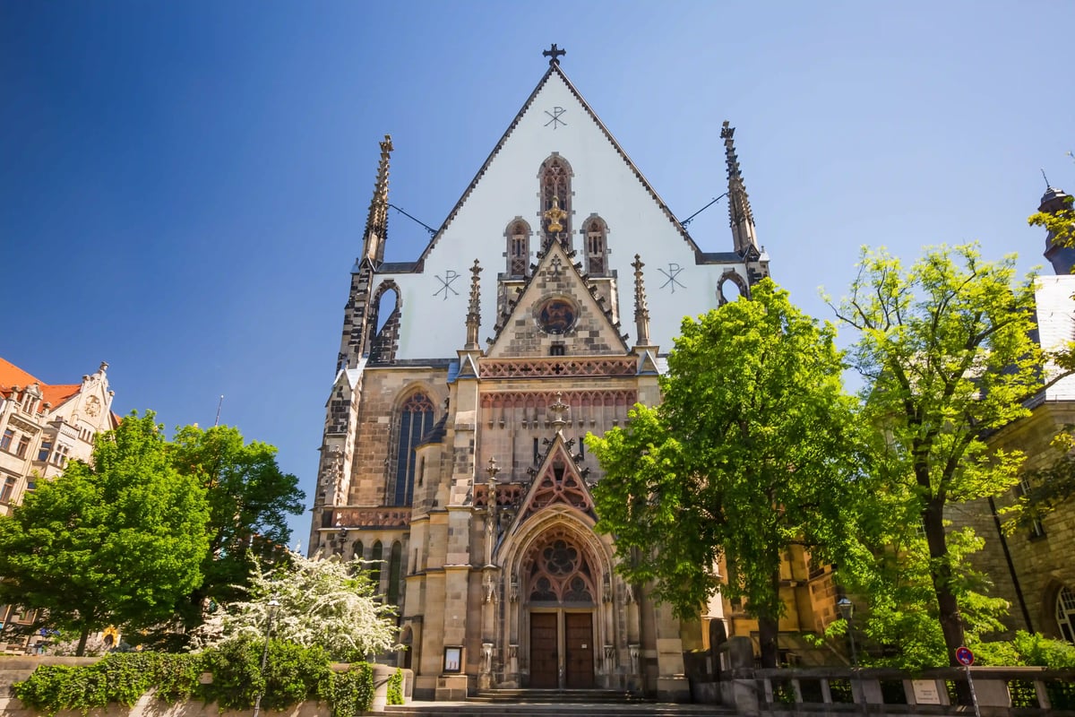 Thomaskirche in Leipzig mit gotischer Fassade und grünen Bäumen.