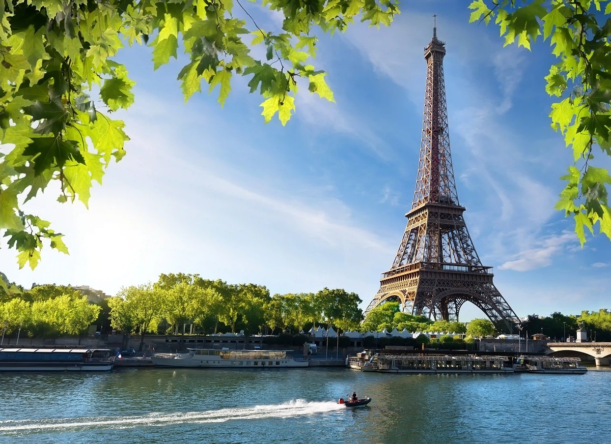 Eiffelturm in Paris mit Blick über die Seine, Booten und grünen Uferbäumen
