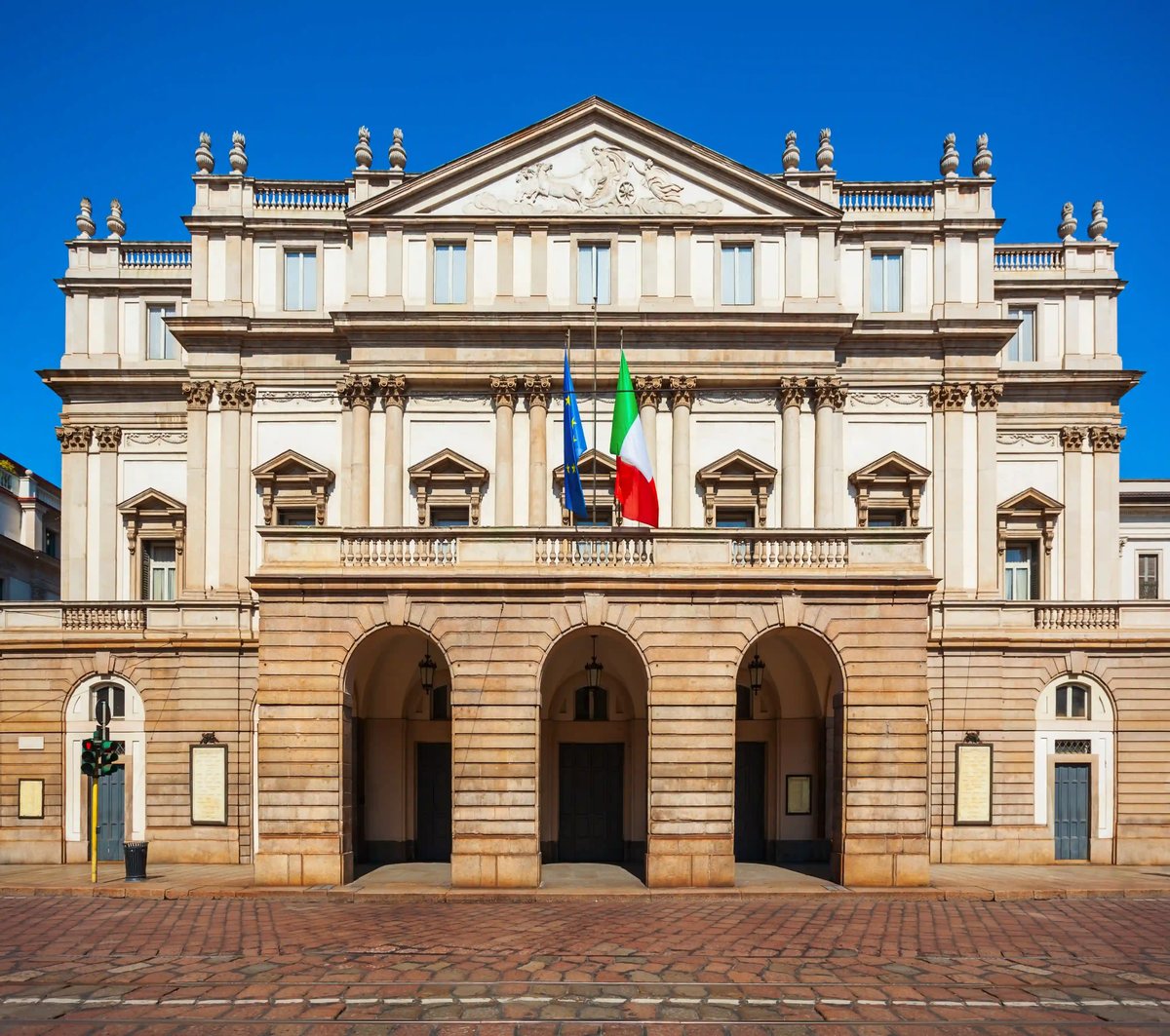 Die weltberühmte Mailänder Scala mit klassizistischer Fassade und italienischer Flagge.