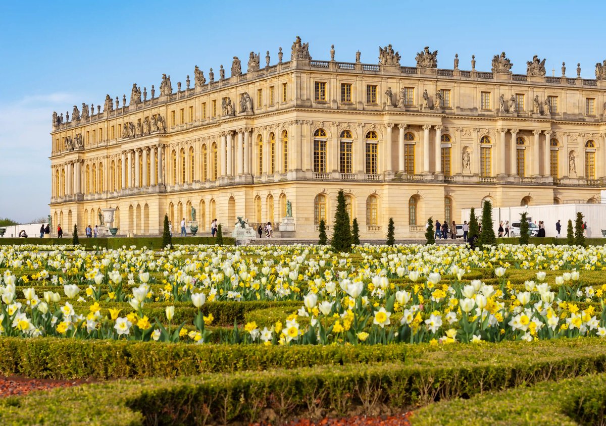 Schloss Versailles mit prachtvoller Gartenanlage und Frühlingsblumen im Vordergrund.