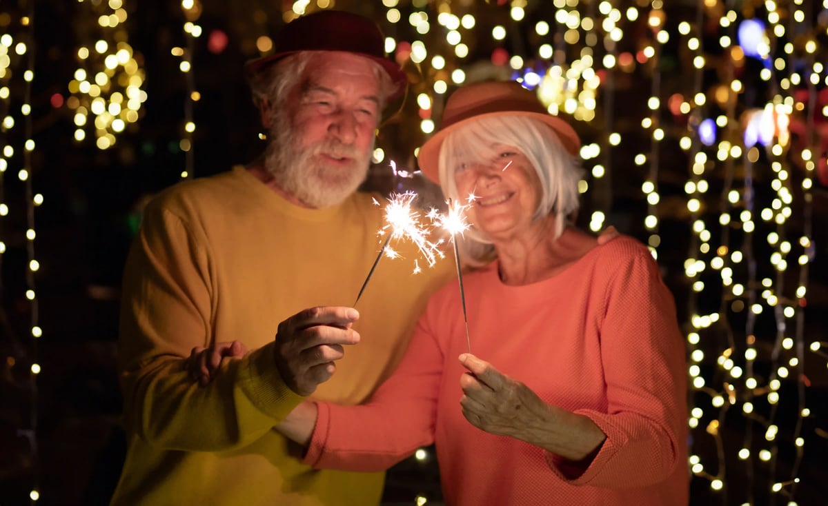 Älteres Paar hält Wunderkerzen vor festlicher Lichterdekoration und lächelt in die Kamera