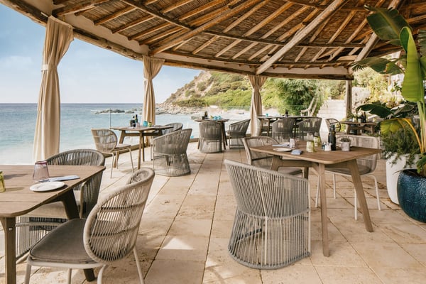 Offene Restaurantterrasse mit gedeckten Tischen und Blick auf das Meer in einer sardischen Bucht