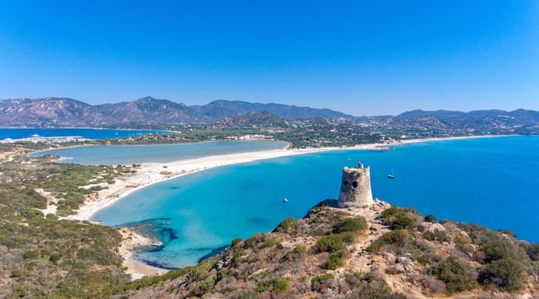Panoramablick auf die Bucht von Villasimius mit Sandstrand, blauem Meer und historischem Wachturm auf einem Hügel