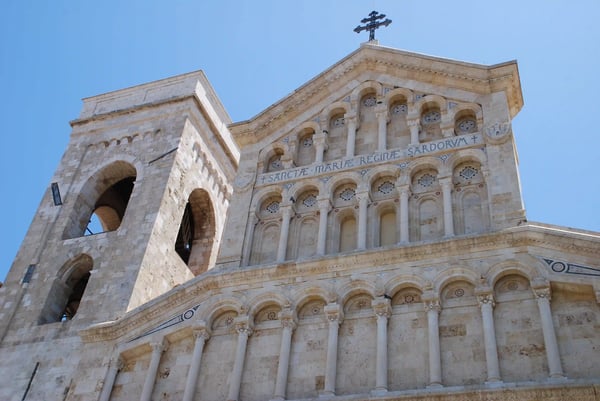 Fassade der Kathedrale Santa Maria in Cagliari mit romanischen Bögen und Glockenturm vor blauem Himmel
