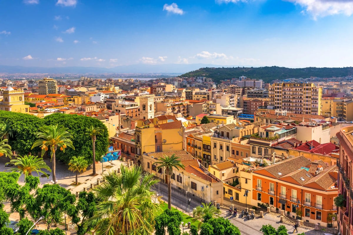 Blick über die sardische Hauptstadt Cagliari mit farbigen Häusern, Palmen und Hügellandschaft