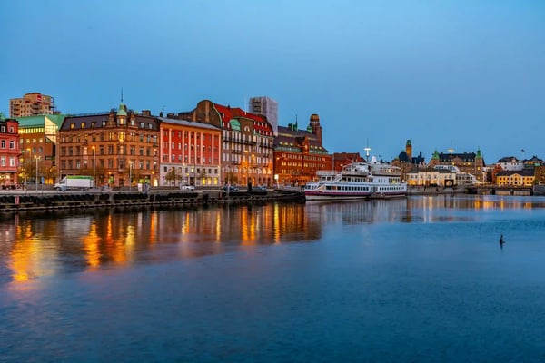 Abendliche Uferpromenade in Malmö mit beleuchteten historischen Gebäuden, Hafenbooten und Spiegelungen der Lichter im ruhigen Wasser