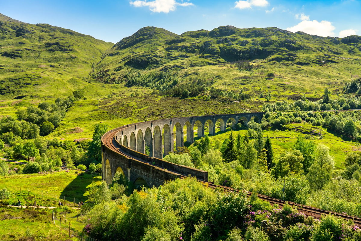 Glenfinnan Viadukt mit geschwungener Eisenbahnbrücke in grüner Hochlandlandschaft